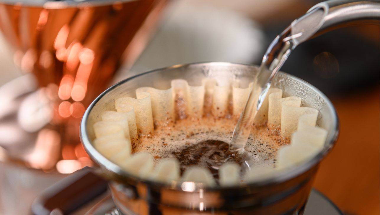 Hot water pouring into french press with filter and coffee grounds